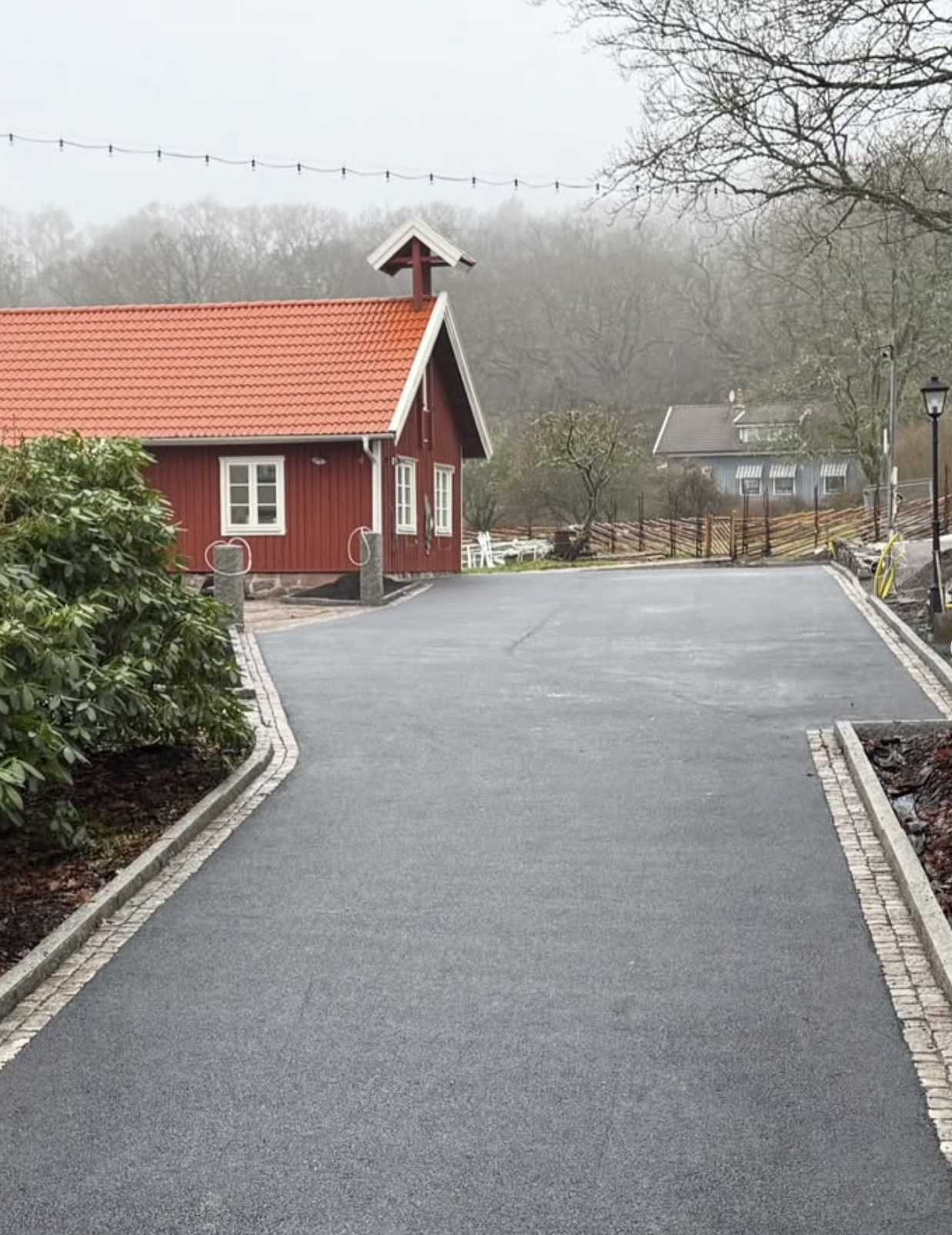Nyasfalterad uppfart vid rött hus med kantsten i granit, dimmig dag