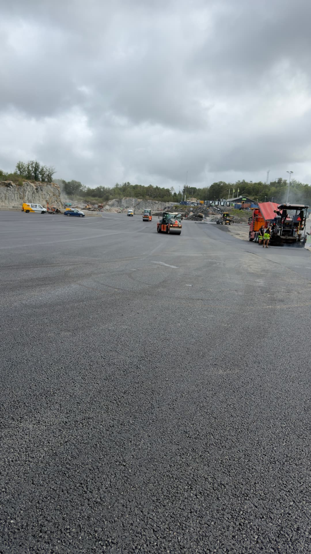 Asfaltläggare och vältar under utläggning av stor industriyta vid bergtäkt