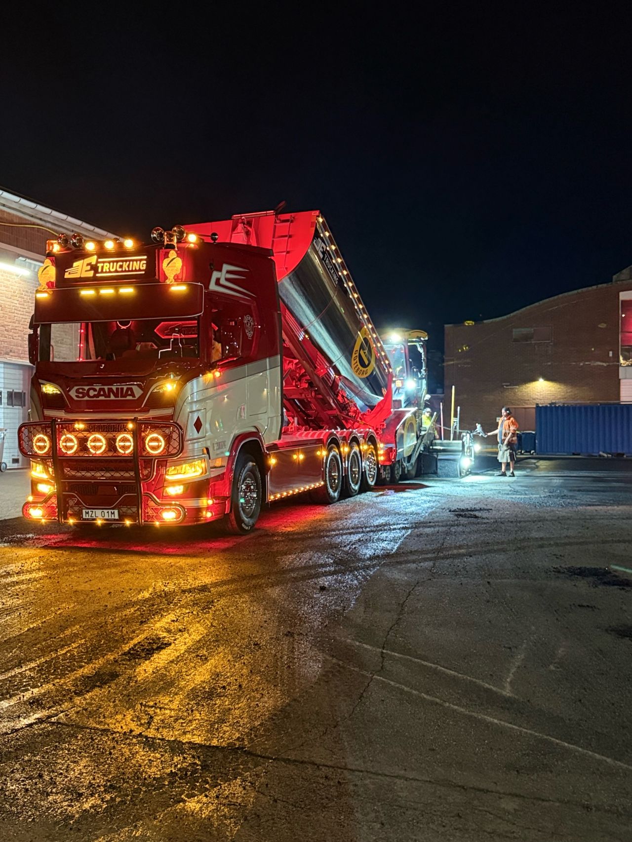 Asfaltläggare och Scania-lastbil i arbete nattetid