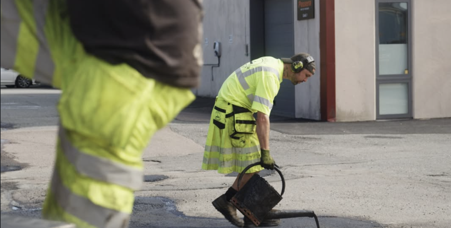 Asfaltarbetare lagar hål i asfalt vid industribyggnad