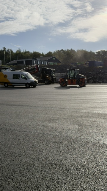 Servicebil och hjullastare vid asfaltarbete på industriområde