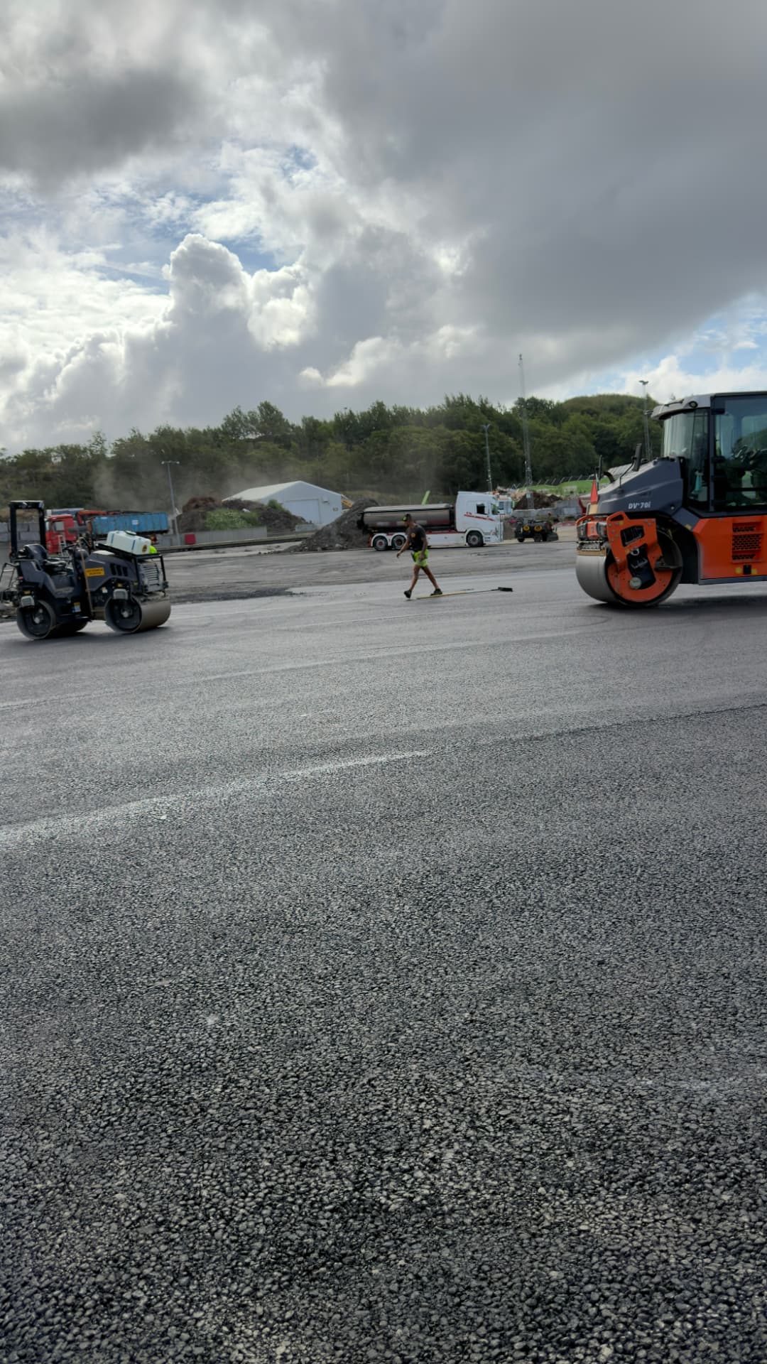 Vältar och arbetare som sopar nylagd asfalt på stor entreprenad